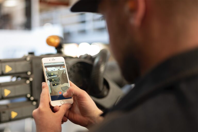 A man holding a cell phone that displays a live video feed, demonstrating using robot field ops via his phone.