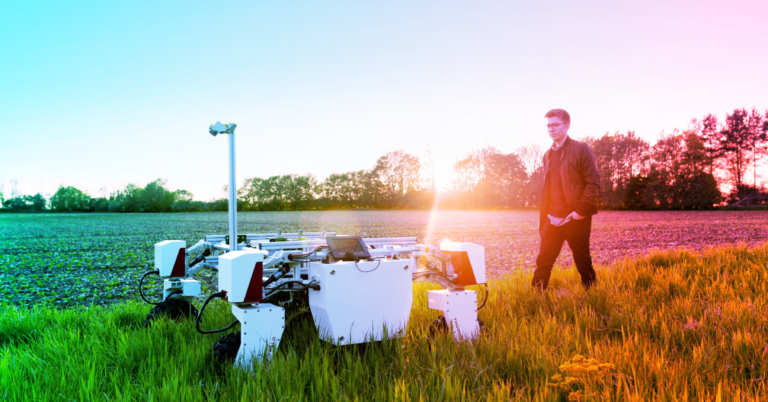 A worker walks alongside a robot in a field.